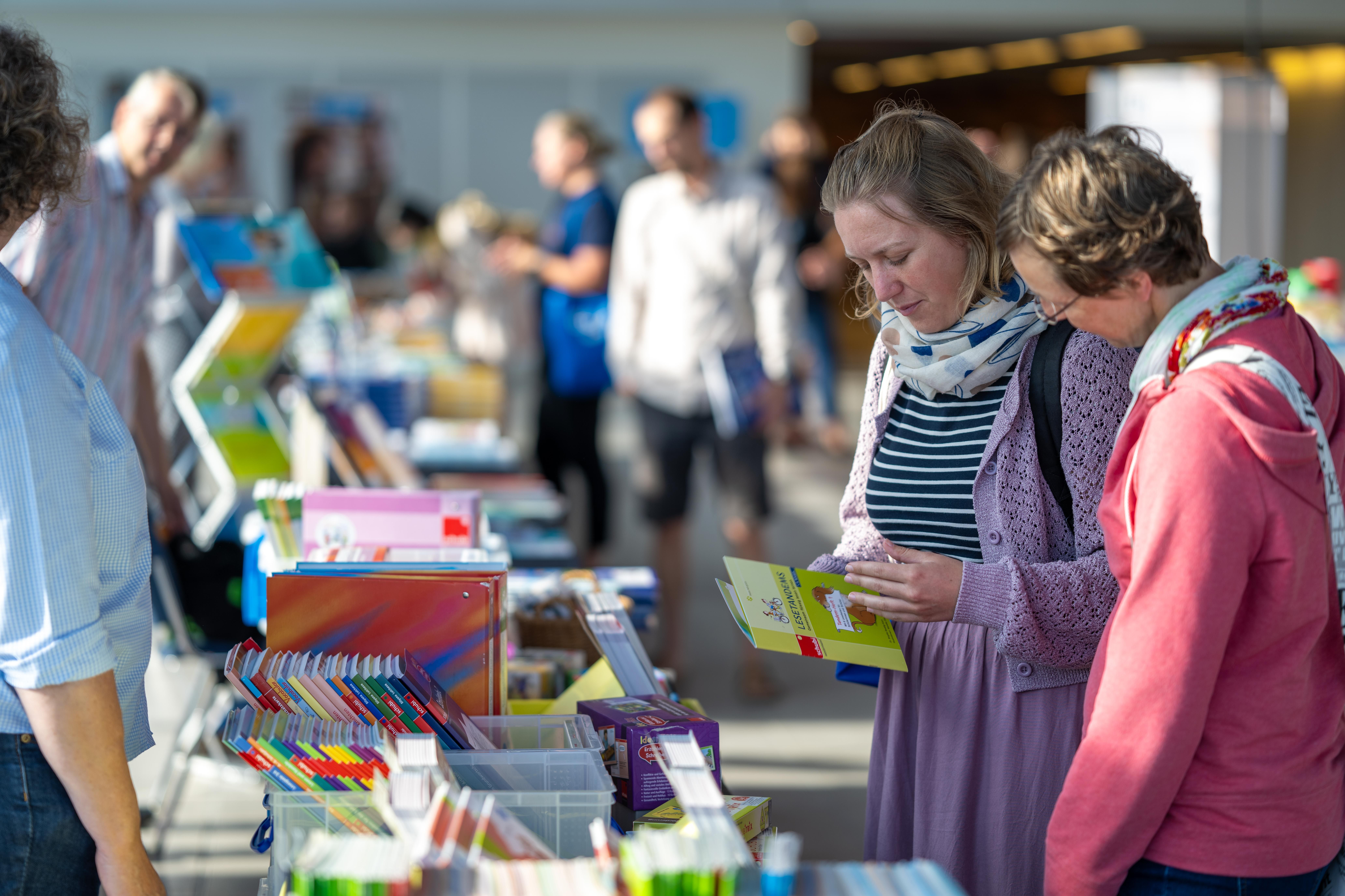 Zwei Frauen sehen sich an einem Verkaufsstand ein Buch an.
