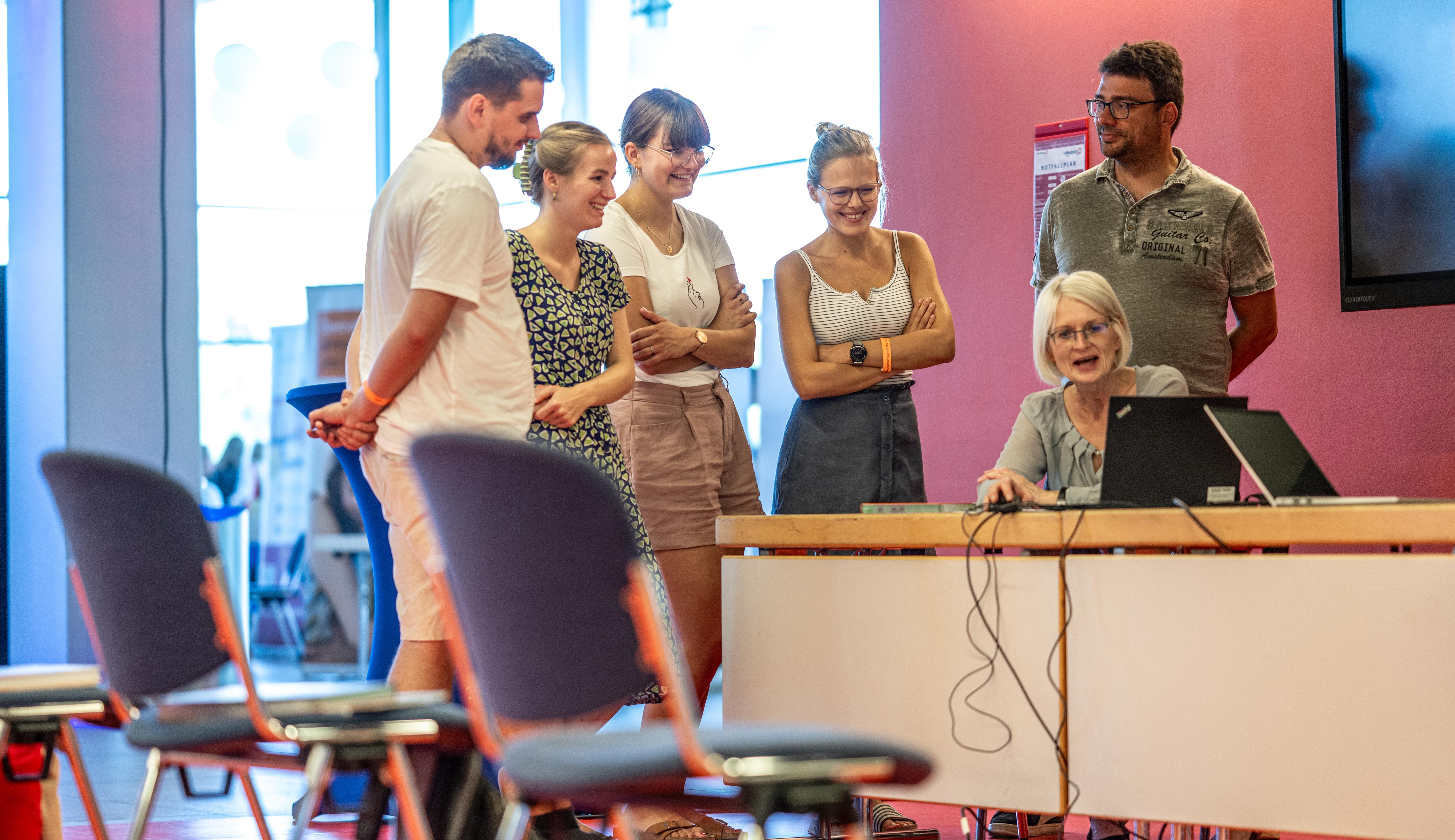 Eine Frau zeigt anderen Menschen etwas auf einem Computerbildschirm.