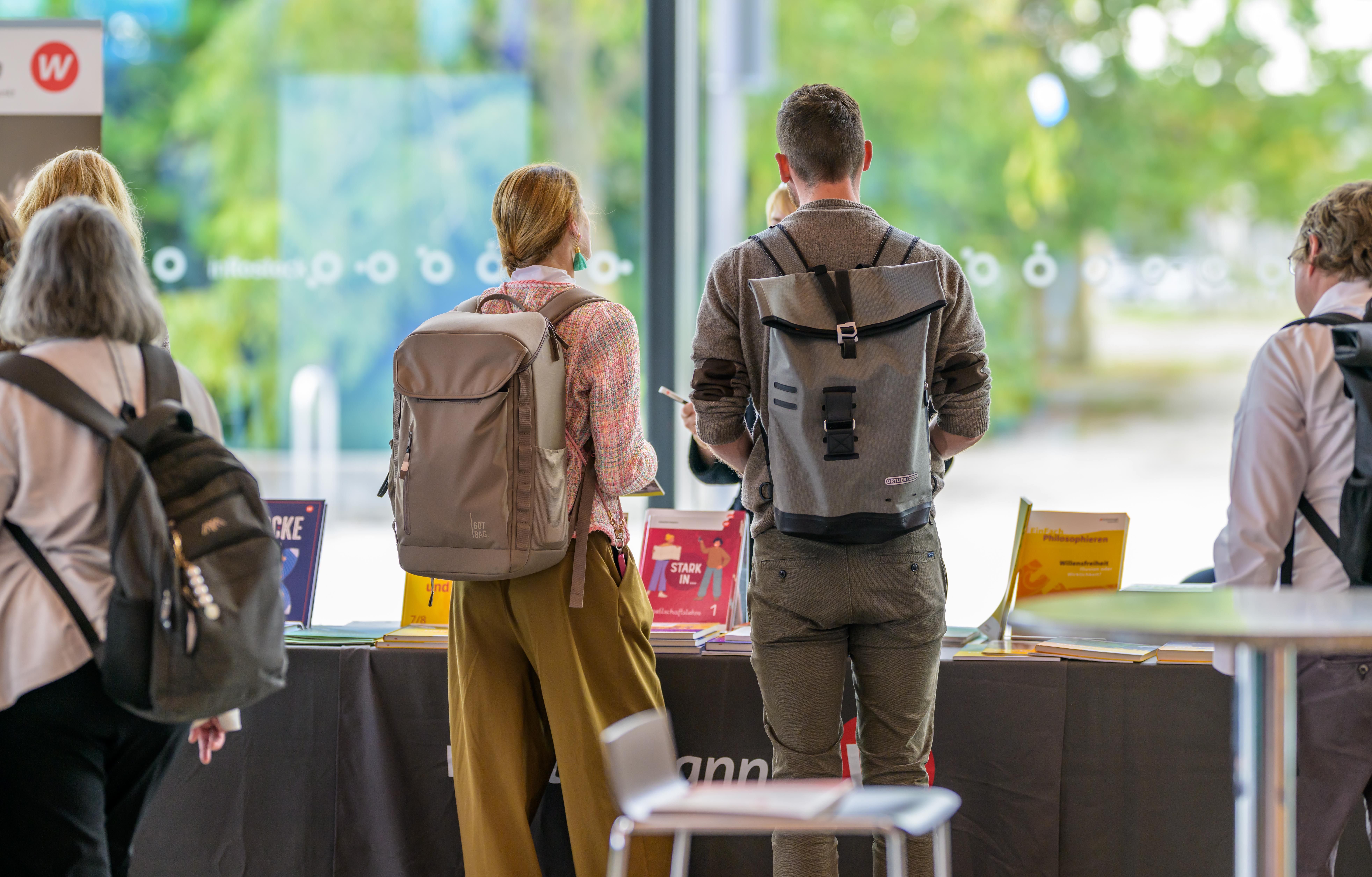 Ein Mann und eine Frau mit großen Rucksäcken schauen an einem mobilen Messestand Informationsmaterial an.