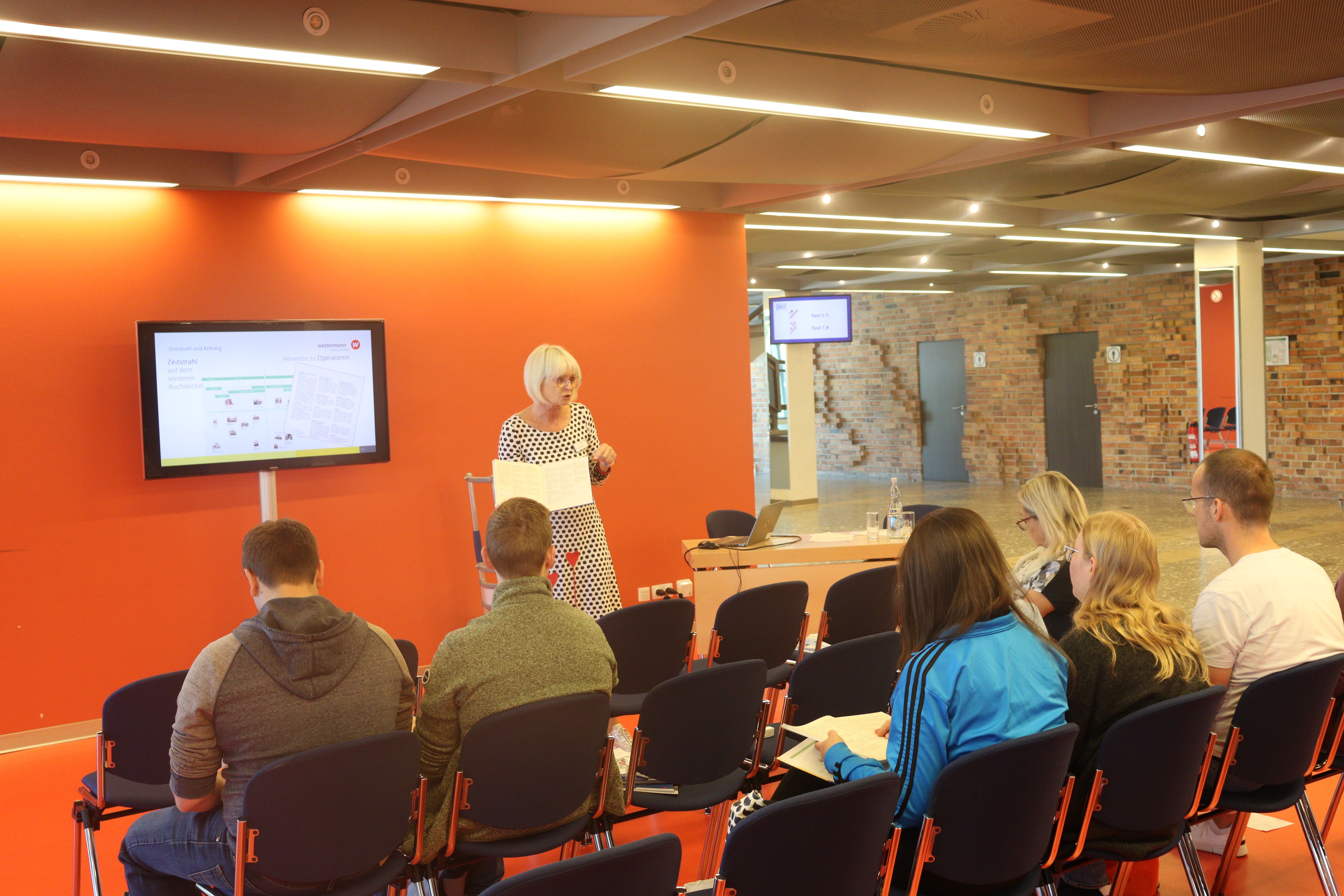 Eine Referentin steht vor Zuschauerinnen und Zuschauern.